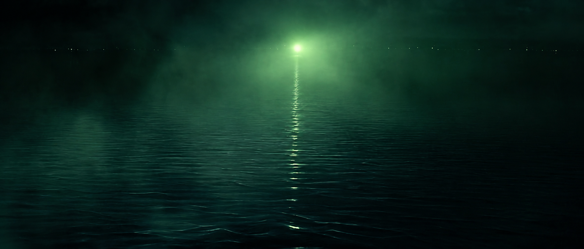 A distant green light glowing through fog and reflecting across dark water.